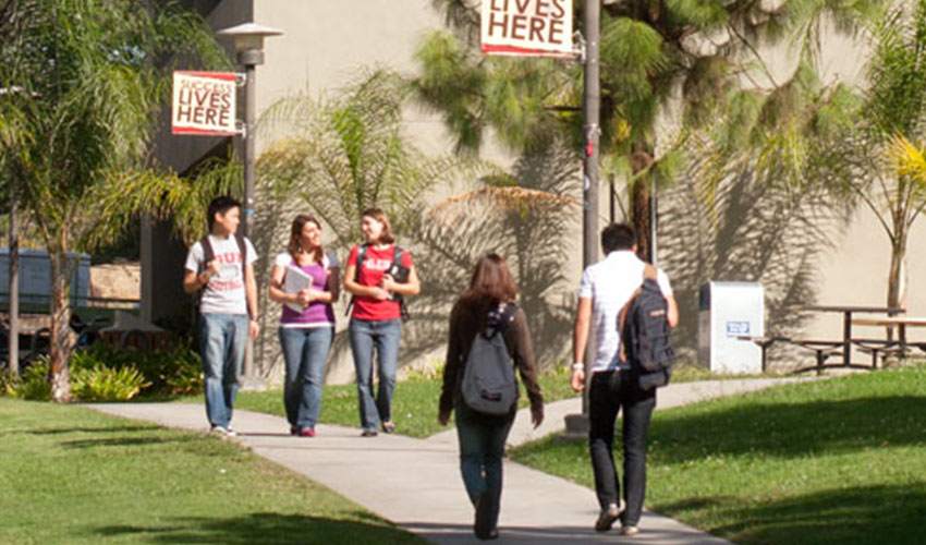 A diverse group of students walking on a sidewalk next to a building, appearing cheerful and engaged in discussion