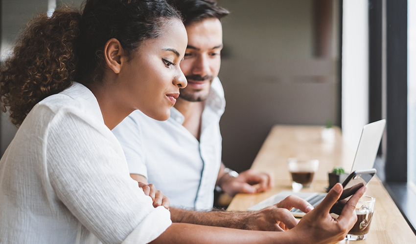 A man and woman sit at a table, focused on a laptop screen, sharing ideas and collaborating together.