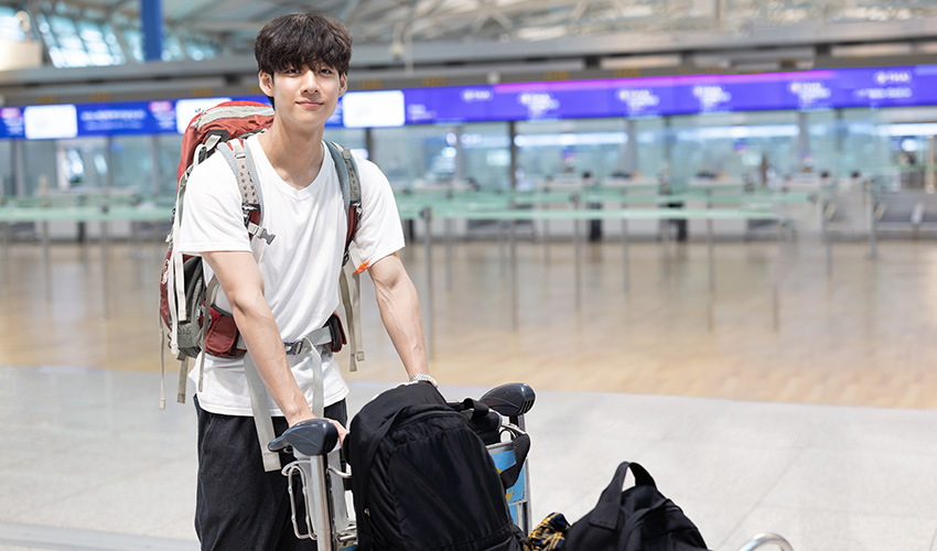 A student stands at the airport with luggage, ready for an exciting journey ahead.