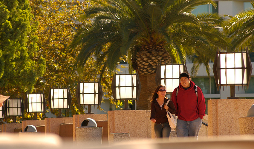 A couple of CSUN students strolls down a walkway in front of the library.