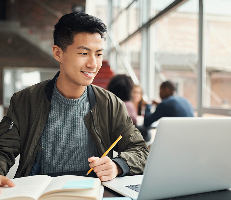 A CSUN student smiles while seated at a table, working on a laptop, embodying a moment of academic engagement.