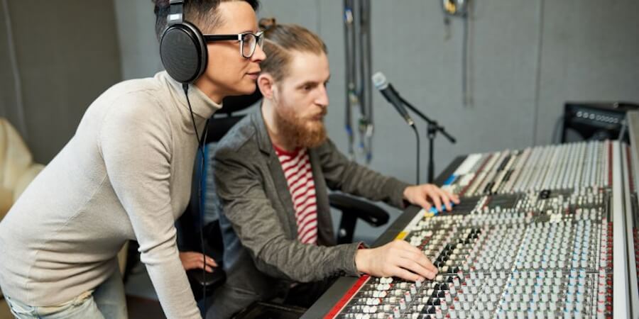 A music industry manager working with a sound recording technician in a sound booth.