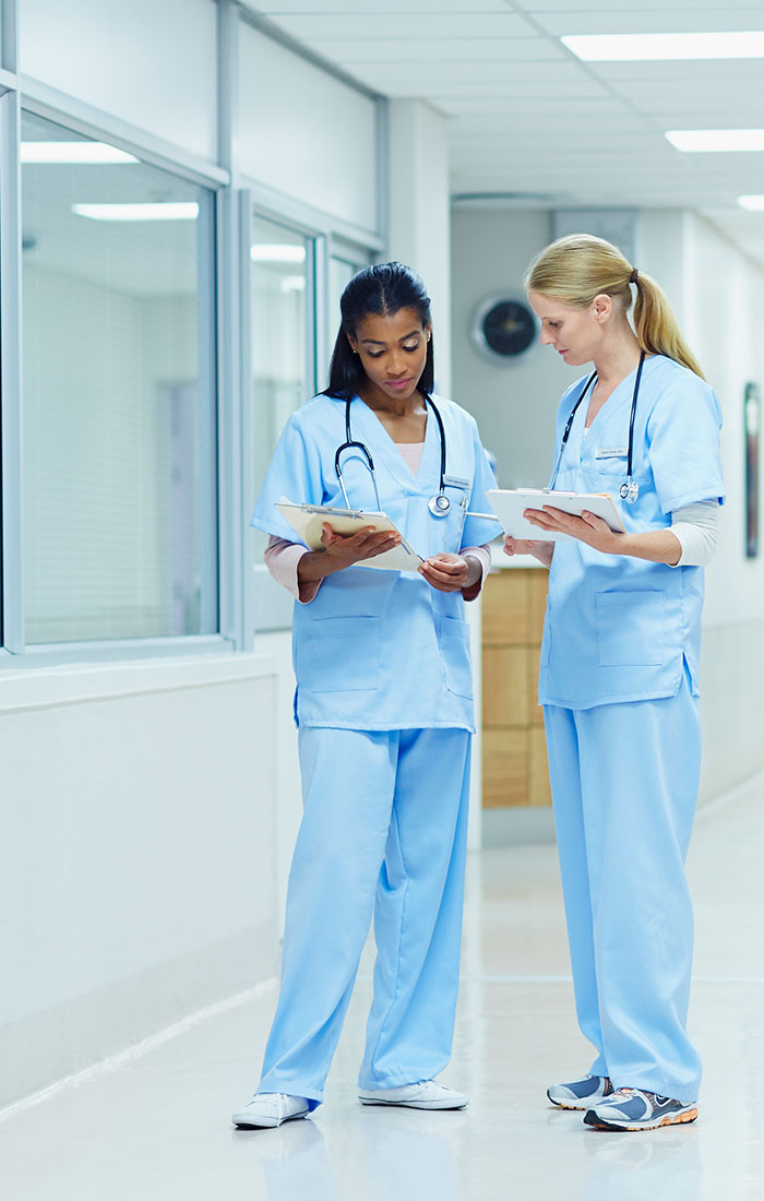 Two young female nurses talking in a hospital corridor.