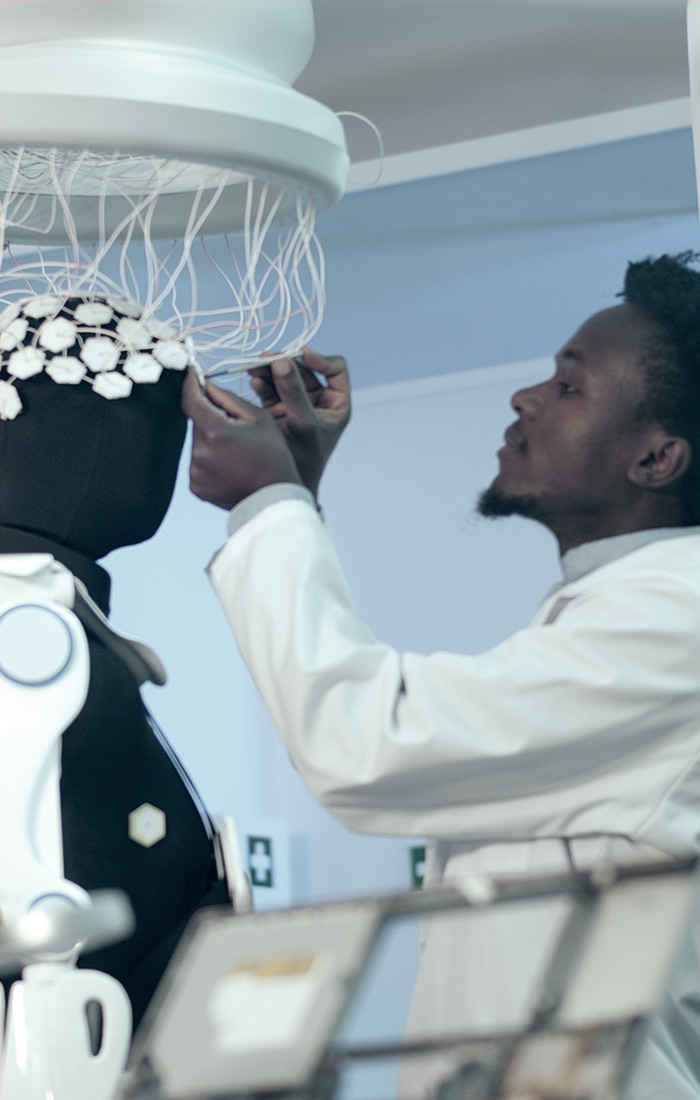 A man in a white coat working on brainwave scanning headset and exoskeleton.