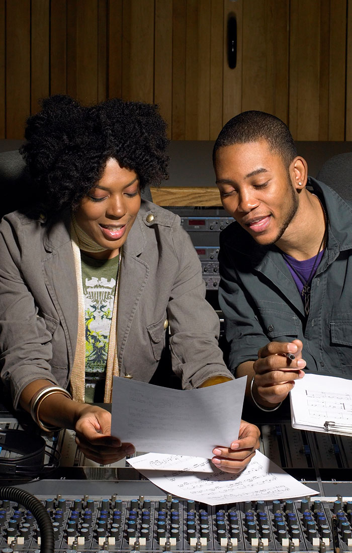 Two music producers are discussing business in a recording studio.