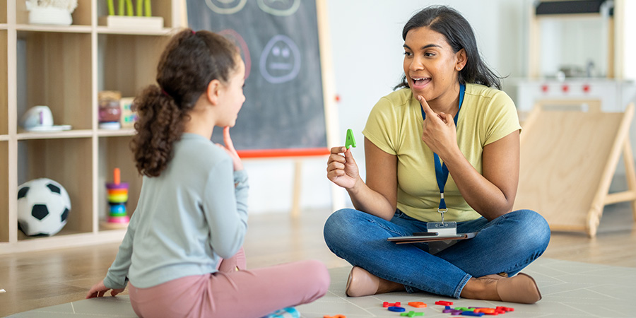 A speech-language pathologist works with a child sitting in a classroom.