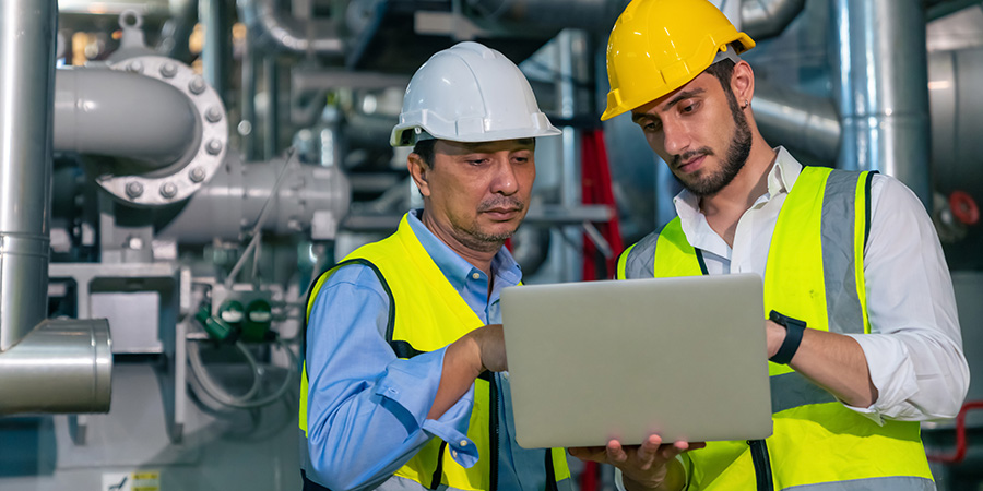 Two engineers review data on a laptop at a worksite.