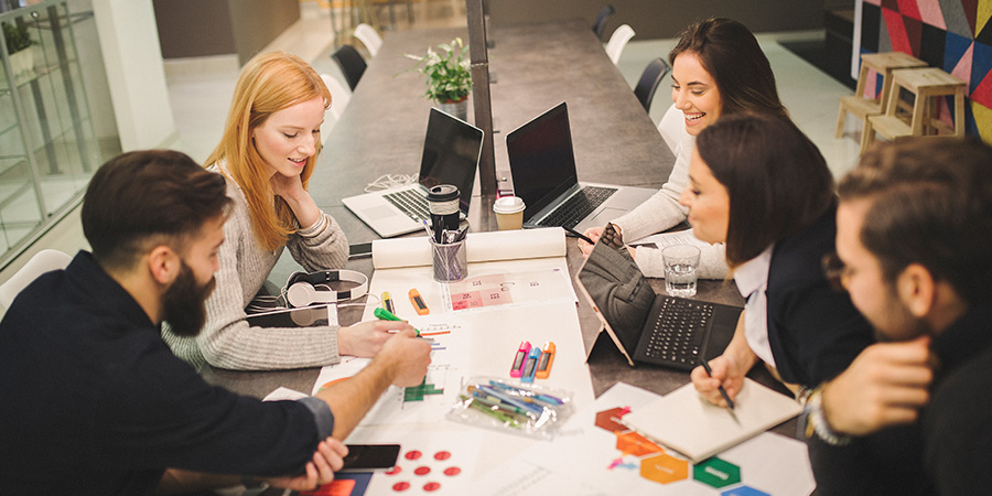 A group of design strategy professionals sitting at a table discussing designs on papers and laptops.