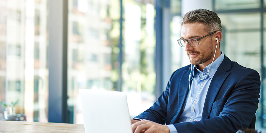 A music distributor sitting at a desk in front of a laptop with headphones on.