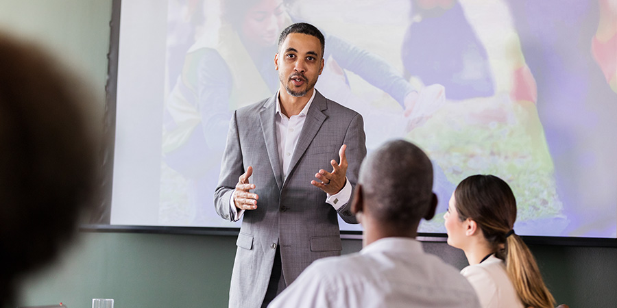 A public sector organization leader standing in front of a screen at a business meeting.