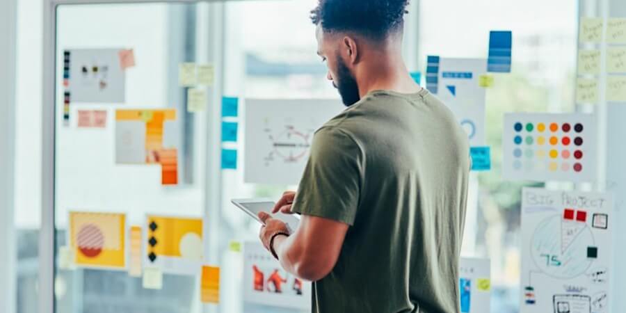 A design consultant uses a tablet while reviewing color schemes on a glass board.