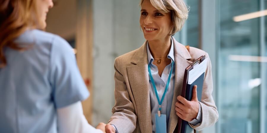 A healthcare administrator shakes hands with a nurse in a hospital corridor.