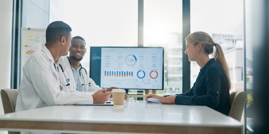 A data visualization specialist reviews some healthcare data with two doctors. 