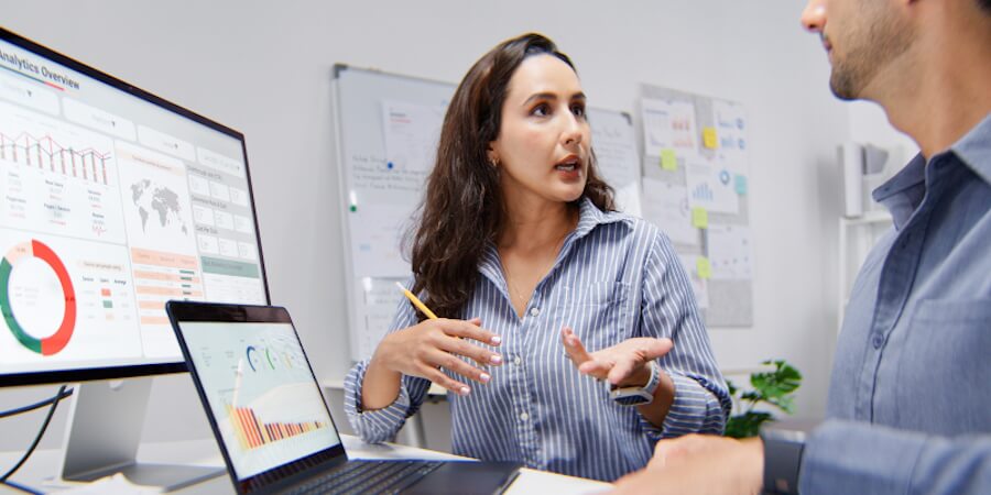 A data analyst explains a data visualization dashboard displayed on a monitor to a colleague.