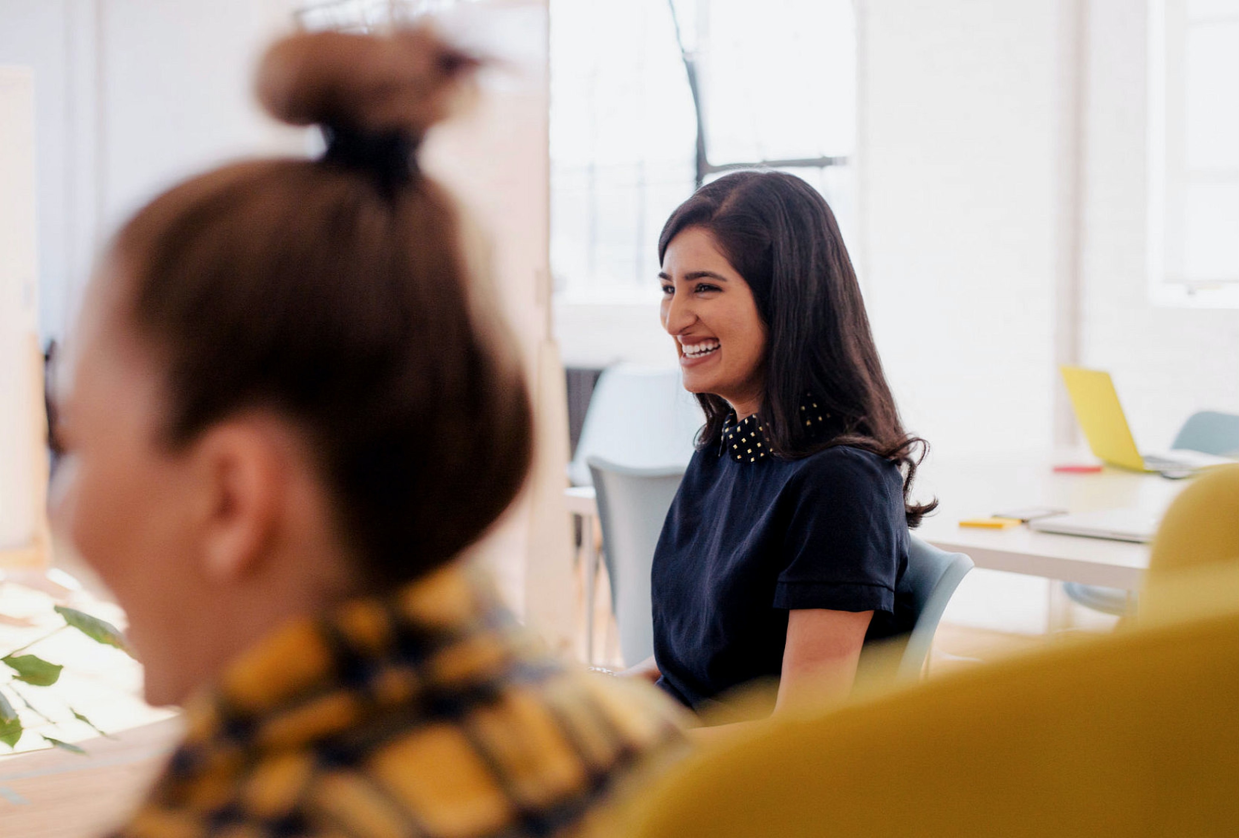 Two female colleagues sitting at a conference table smiling happily