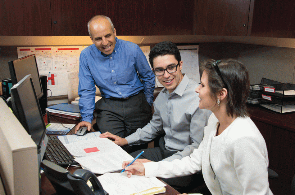 Professor Rafi Efrat (left) works with students in CSUN’s David Nazarian College of Business and Economics to review federal tax procedures. Photo by Lee Choo. Two students working on assignment with professor standing beside them.